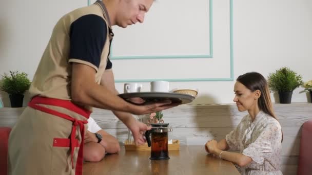 Il cameriere serve il tè saporito a coppia felice a tavolo in caffè — Video Stock