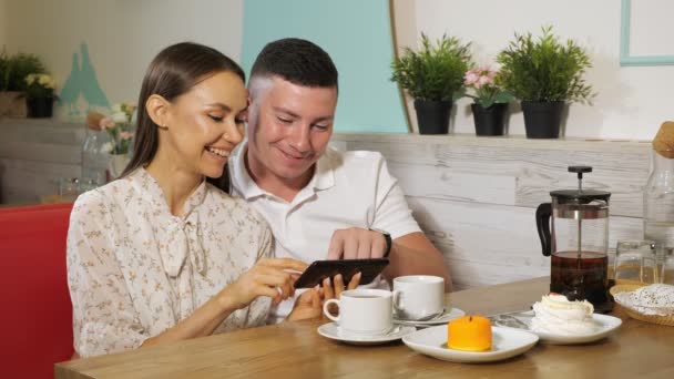 Girl and guy looks at mobile phone at table in sweet shop — Stock Video