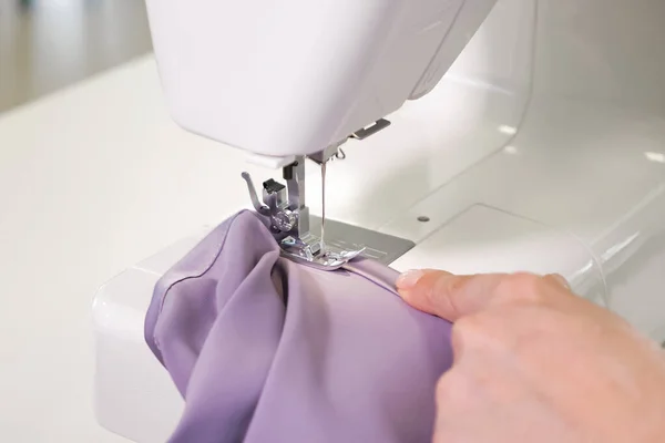 Seamstress works at sewing machine makes straight seams on cloth, hands closeup.