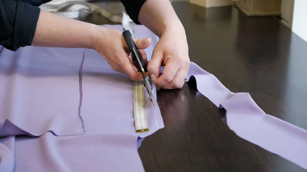 Tailor cuts cloth uses scissors follow chalk markings of pattern, closeup hands.