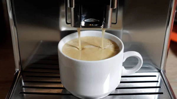 Кофе наливает в чашку из современной кофеварки в номере — стоковое фото