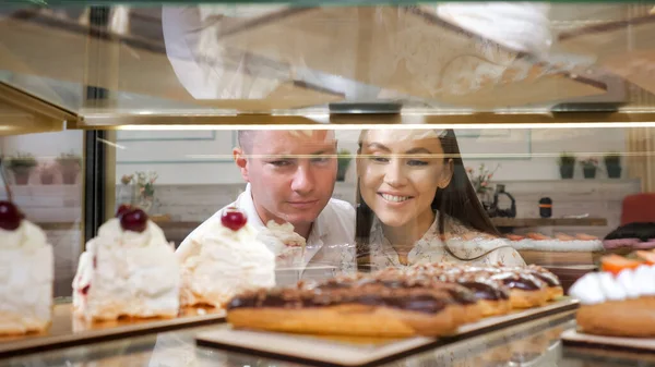 Счастливая пара выбирает вкусные торты в витрине магазина — стоковое фото