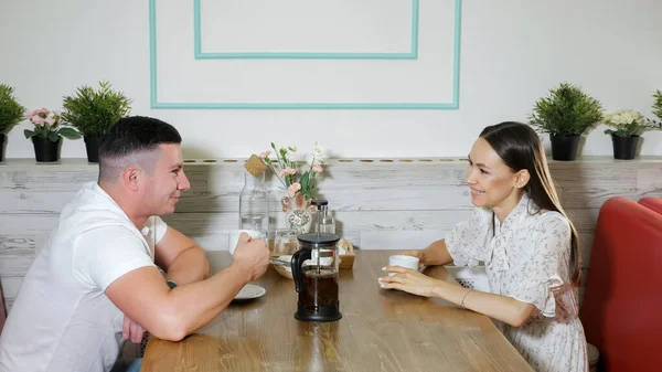Mladý pár hovoří a pije čaj u dřevěného stolu v kavárně — Stock fotografie
