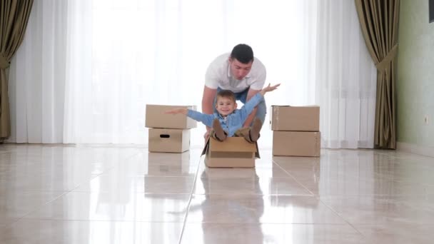 Vader draagt witte shirt rijdt lachende zoon in ambachtelijke doos — Stockvideo