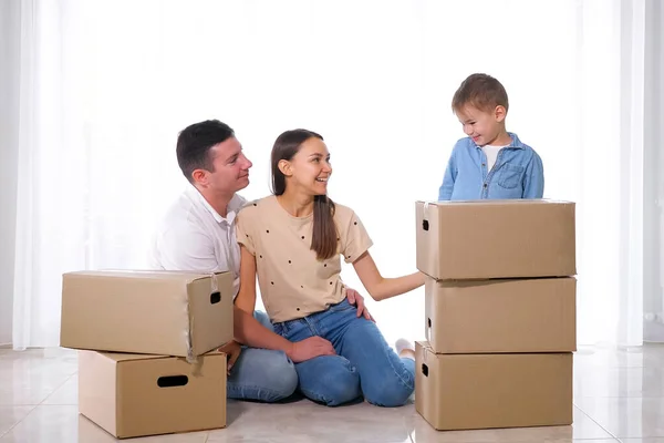 Fia áll dobozok mögött közel szülők ül a padlón — Stock Fotó