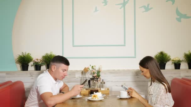 Man en vrouw gebruiken telefoons aan tafel met desserts in café — Stockvideo