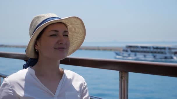 Красива жінка в елегантному солом'яному капелюсі сидить на корабельній палубі — стокове відео