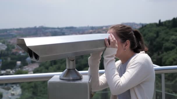 Woman looks through binoculars exploring cityscape along bay — Stock Video