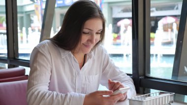 Kafedeki masada telefonu olan esmer bir kadın.