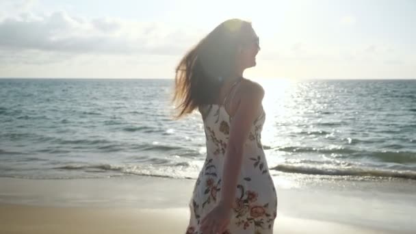 Улыбающаяся женщина в платье бежит по пустому морскому пляжу к волнам — стоковое видео