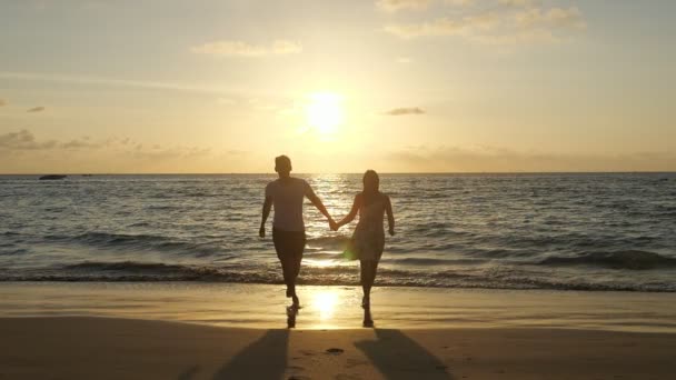 Silhuetas de casal correndo ao longo da praia contra ondas — Vídeo de Stock