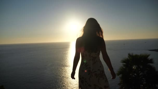 Frau im Sommerkleid hebt bei Sonnenuntergang am Strand die Hände — Stockvideo