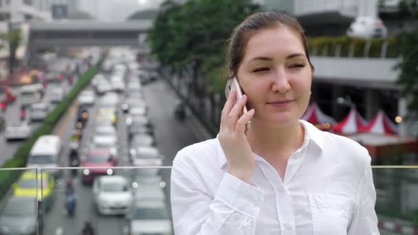 Mujer joven habla en un teléfono inteligente blanco y sonríe alegremente — Vídeo de stock