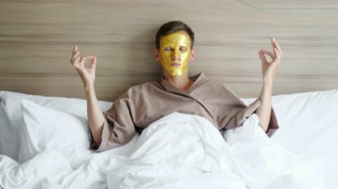 Altın maskeli adam otelde yatakta meditasyon yapıyor.