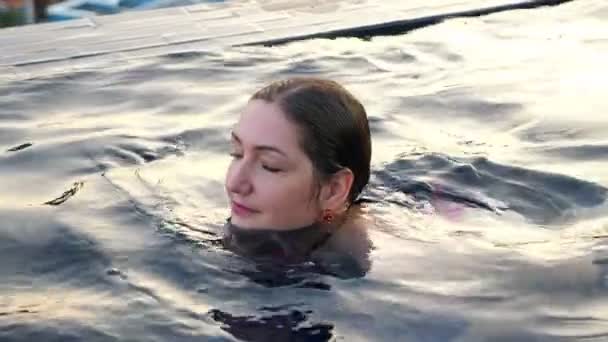 Bela morena em maiô nada na água da piscina azul — Vídeo de Stock