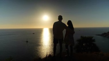 Günbatımında okyanus kıyısında romantik çift kucaklaşması.