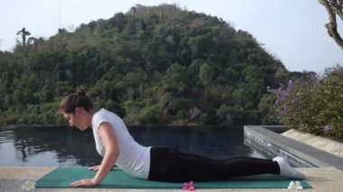 Spor üniformalı genç bir kadın havuz kenarında esneyerek geziyor.