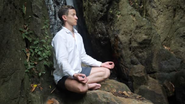 Beau jeune homme médite sur le rock en position de lotus de yoga — Video