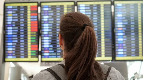 Брюнетка рассматривает расписание вылетов в терминале аэропорта — стоковое фото