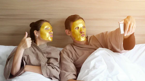 Famiglia con maschere viso fa selfie in morbido letto in hotel — Foto Stock