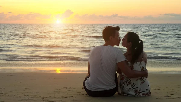 Encantadora pareja joven abrazos y besos sentado en la playa del océano — Foto de Stock