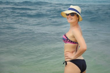 Denizin arka planında şapkalı ve bikinili bir kadın
