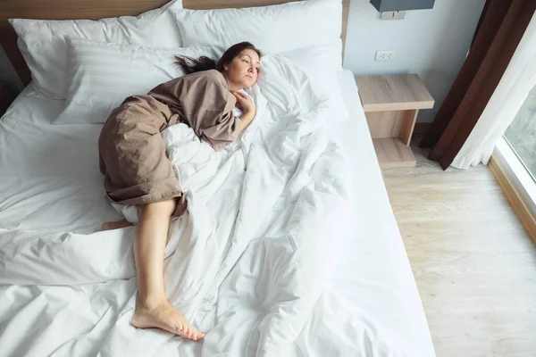 Mujer en albornoz descansa sobre una cama suave con manta y almohadas — Foto de Stock