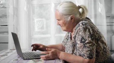 Laptop klavyesinde zayıf tıkırtılar gören yaşlı bir kadın.