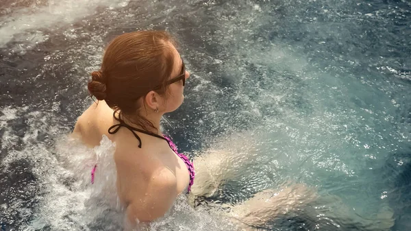 Morena senta-se em azul ao ar livre água da piscina de hidromassagem com espuma branca — Fotografia de Stock