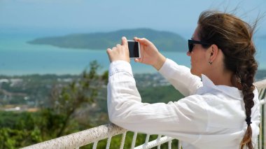 Beyaz bluzlu esmer ve siyah güneş gözlüklü kız fotoğraf çekiyor.