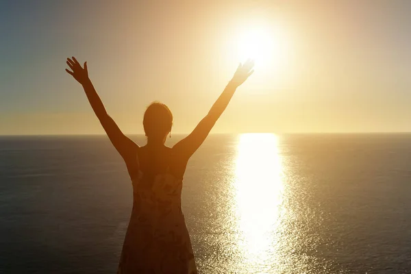 Femme en robe d'été lève les mains sur la plage au coucher du soleil — Photo