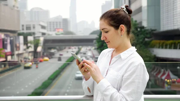 Barna, fehér típusú okostelefon a hídon utca felett — Stock Fotó