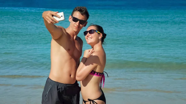 Sonriente feliz pareja hace selfie en soleado playa cerca de azul océano — Foto de Stock