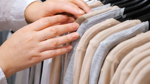 Las manos femeninas clasifican los pullovers de algodón en una percha en una tienda de ropa . — Foto de Stock