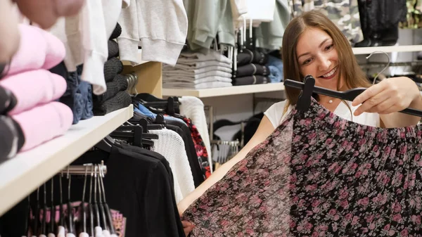 Morena mujer inspecciona plisado negro falda de flores en la tienda — Foto de Stock
