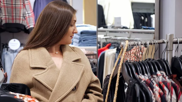 Mujer joven en un abrigo beige cálido se para frente a un espejo en una tienda — Foto de Stock