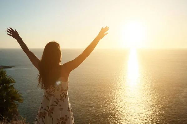 Femme en robe d'été lève les mains sur la plage au coucher du soleil — Photo