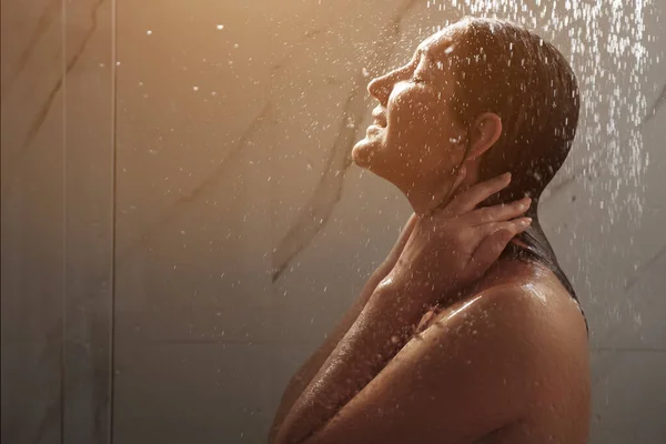 Joven mujer corre las manos en la cara de pie bajo la ducha agua —  Fotos de Stock