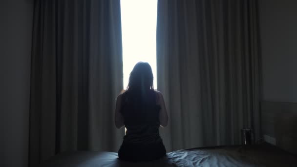 Woman stretches sitting on bed near window in hotel room — Stock Video