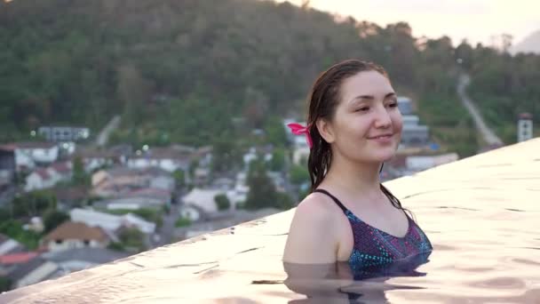 Morena com flor roxa no cabelo olha em volta com sorriso — Vídeo de Stock