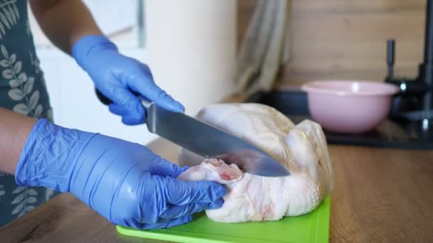 Неузнаваемая женщина в перчатках вырезает целую курицу на кухне. — стоковое видео