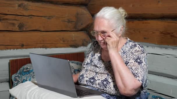 Femme âgée avec un ordinateur portable enlève ses lunettes. Mouvement lent — Video