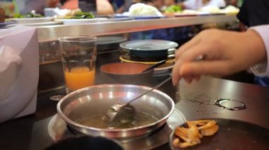 Kadın açık büfedeki deniz ürünleri çorbasını tabaklarla hareket eden bir taşıyıcının arka planına karşı hazırlıyor.