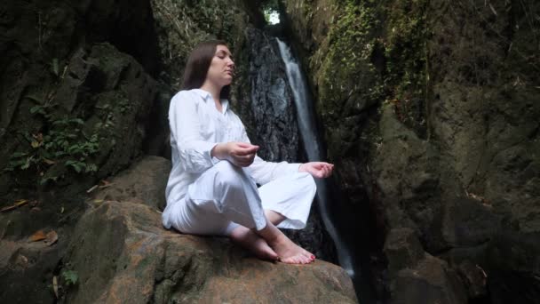 Concentrated young woman sits with closed eyes in lotus pose — Stock Video