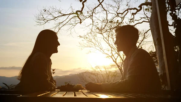 Jovem casal em uma mesa de café em um belo fundo pôr do sol — Fotografia de Stock