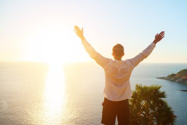 Gün batımında deniz üzerinde elleri havada beyaz gömlekli bir adam. Arkadan bak.