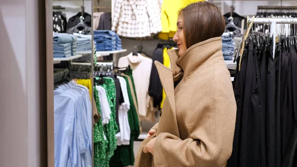 Fiatal nő hosszú, túlméretezett kabátban egy tükör előtt egy boltban. — Stock Fotó