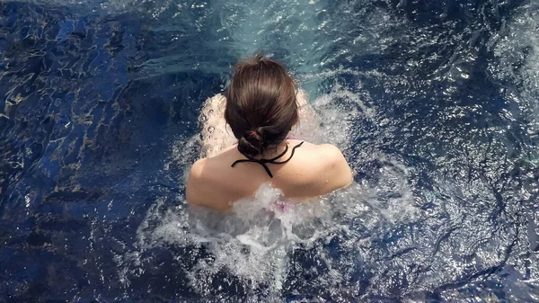 Brunette se trouve dans l'eau de piscine d'hydromassage extérieure bleue avec mousse blanche — Photo