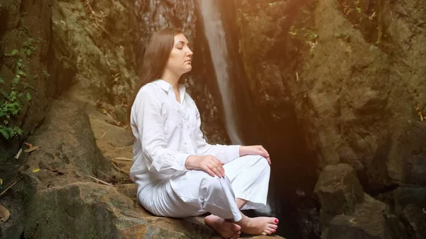 Donna medita in posizione di loto sulla roccia contro cascata — Foto Stock
