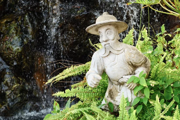 Plaster statue of a man with a beard in a hat among the fern